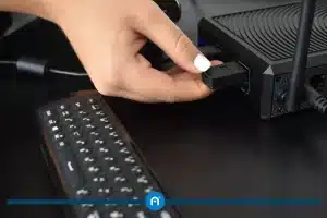 A hand inserts a USB flash drive into a port on a black electronic device, with a keyboard nearby on a black surface—perfect for setting up the ultimate video conferencing experience.