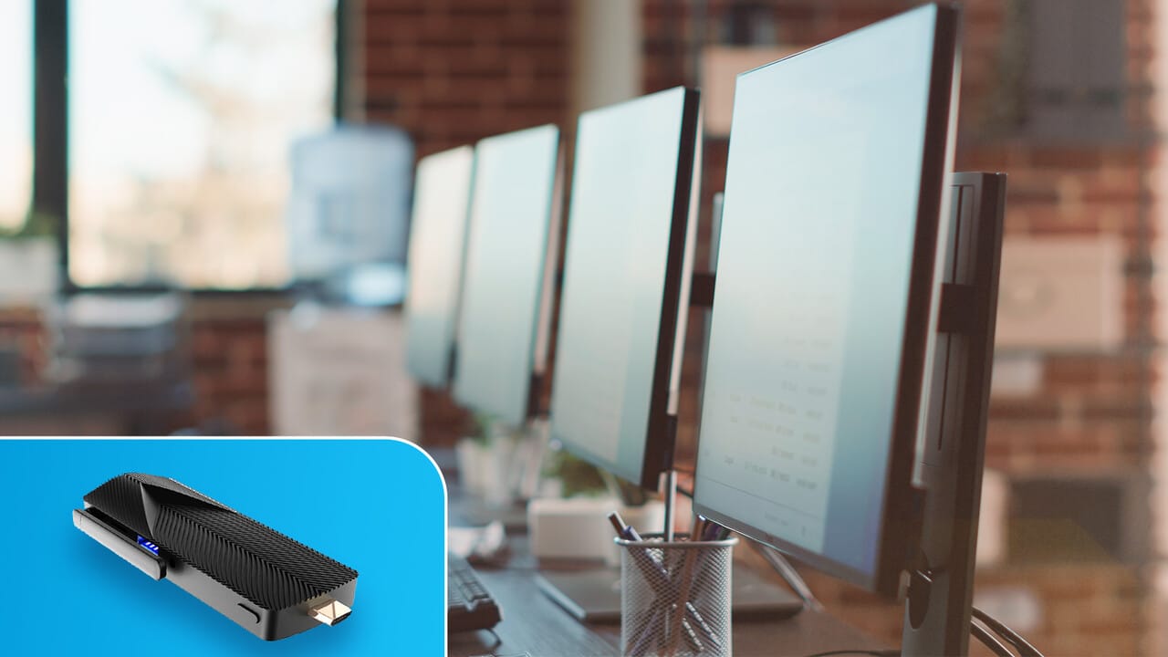 Four computer monitors on a desk in a modern office, displaying graphs and data, with a small edge device showcased in the foreground.