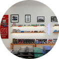 Shelves displaying model cars, boxed sets, and related merchandise against a white wall with framed pictures above and a red sign on the left.