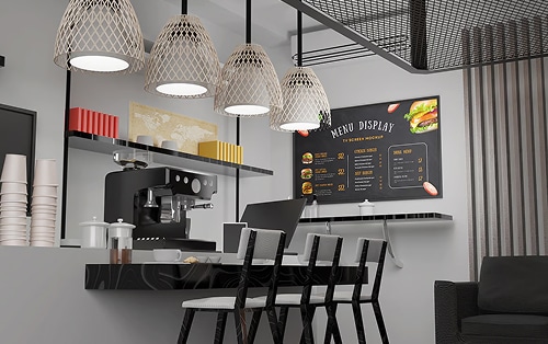 Modern cafe interior with a coffee machine, stools at a black counter, hanging lights, and a digital menu display on the wall.