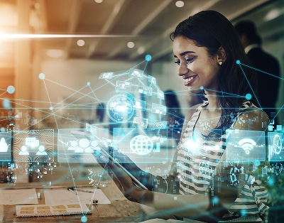 A woman sits at a desk using a tablet, with digital network and technology icons overlaid, representing connectivity and modern communication.