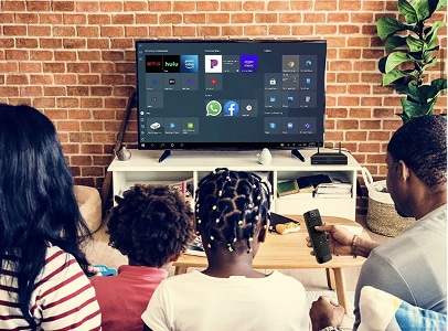 A family of four sits on a couch facing a TV with various streaming and app icons displayed on the screen in a living room.
