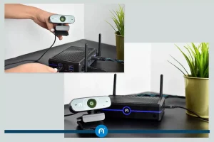 A person connects a webcam to a black electronic device with antennas on a desk; the device is later shown powered on next to a potted plant.