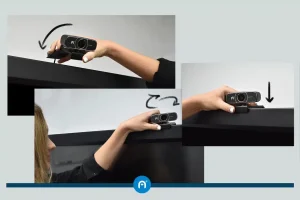 A person mounts a webcam onto the top edge of a monitor in three sequential steps.