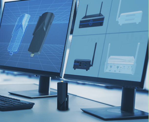 Two computer monitors display technical diagrams of electronic devices; a small black device sits on the desk in front of the monitors.
