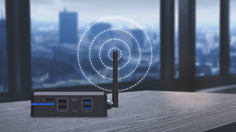 A small wireless router with antenna sits on a desk, emitting signal waves, with a blurred cityscape visible through the window in the background.