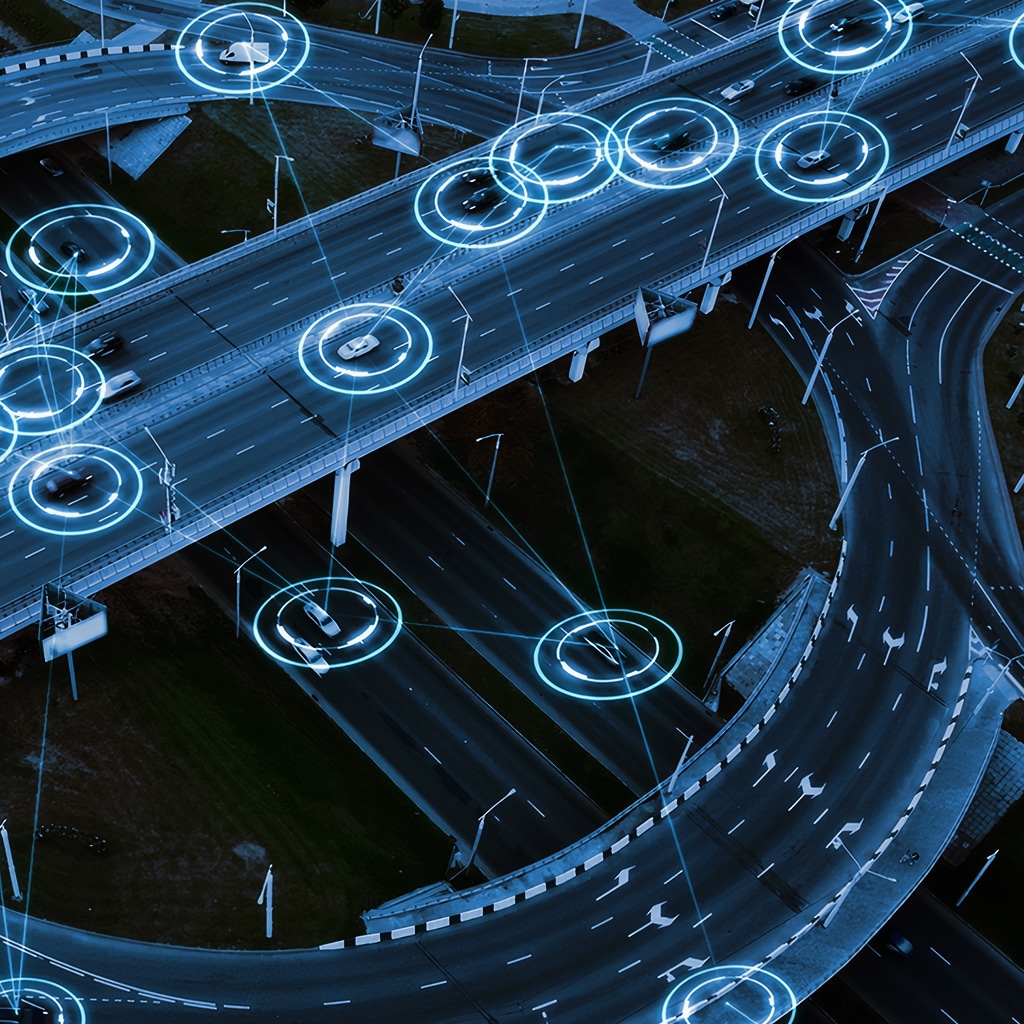 Aerial view of multi-level highways with digital blue circles highlighting vehicles, illustrating smart transportation or connected car technology.